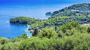 A coastal landscape with a clear view of the sea, a small island, and a hilly area with scattered buildings.