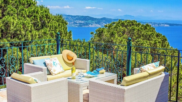 A terrace with wicker furniture, a bottle, and a hat, overlooking a coastal landscape.