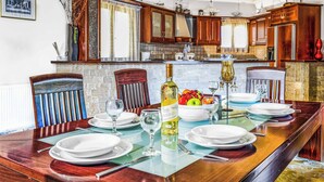 A dining area with a long wooden table set for six, surrounded by wooden chairs. A bottle of wine and a bowl of fruit are on the table.