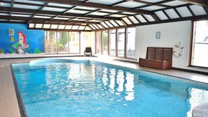 An indoor swimming pool with clear blue water, a mural of a mermaid on the wall, and a wooden bench by the pool. - Delightful 2 bedroom cottage in beautiful Devon countryside, indoor pool & sauna (Tiverton)