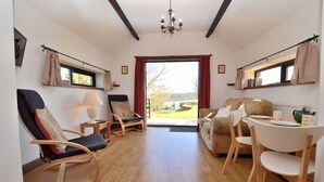 A cozy room with a wooden floor, a sofa, two rocking chairs, a table with a chair, and a window with curtains. - Delightful 2 bedroom cottage in beautiful Devon countryside, indoor pool & sauna (Tiverton)