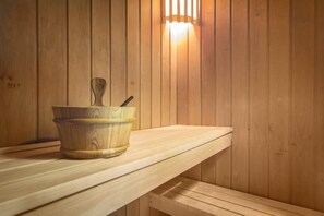 Un banc en bois pour sauna, accompagné d’un seau en bois et d’une brosse.