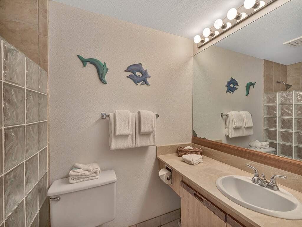 A bathroom with a toilet, sink, and mirror. There are towels hanging on the wall and a shower visible in the reflection.