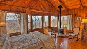 Ein gemütliches Cabin-Zimmer mit einem großen Bett, einem Schaukelstuhl, einem Kamin und großen Fenstern mit Blick auf den umliegenden Wald.