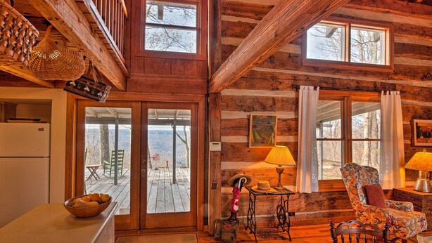 Ein rustikales Blockhaus-Interieur mit Holzwänden, einem Essbereich mit Tisch und Stühlen, einer Küche mit Kühlschrank und einem großen Fenster mit Blick auf eine Terrasse.