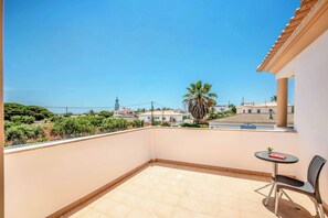 Ein Balkon mit Fliesenboden, einem kleinen runden Tisch und einem Stuhl, mit Blick auf Gebäude und Grünflächen.