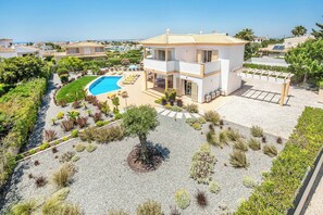 Ein zweistöckiges Gebäude mit Swimmingpool, umgeben von gepflegten Gärten und freiem Blick auf das Meer.