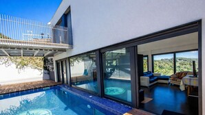 Ein modernes Haus mit Swimmingpool, große Glasfenster, die in einen Wohnbereich mit Blick auf die Landschaft führen.