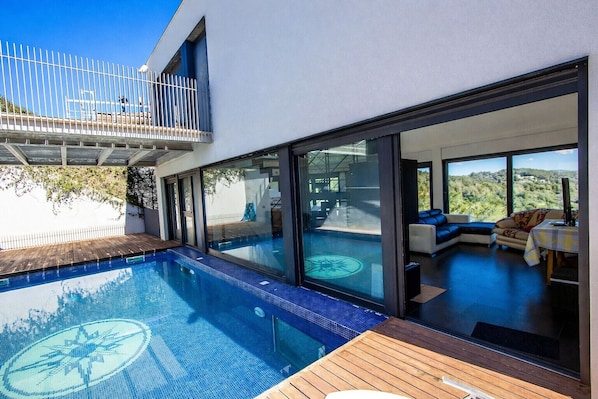 A modern house with a swimming pool, large glass doors leading to a living area with a view of the countryside.