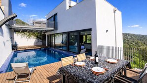 Ein modernes Haus mit Swimmingpool, Essbereich im Freien und einem Balkon.