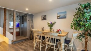 Uma sala de jantar com mesa e cadeiras de madeira, um vaso com flores e uma planta em vaso.
