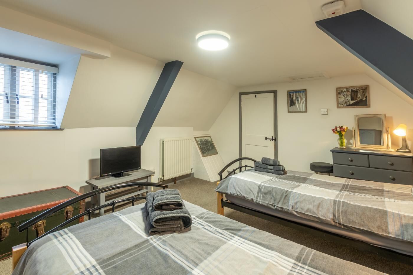 Een slaapkamer met twee bedden, een televisie, een dressoir, een radiator en een raam met zonwering.