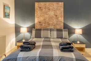 A bed with a plaid bedspread, two pillows, two nightstands with lamps, and a large wall map. - 3 Bed in Appledore (oc-cockle) (Appledore)