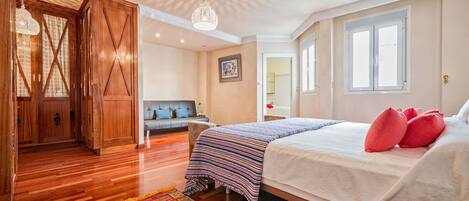 A bedroom with a bed, a sofa, a wooden wardrobe, and a patterned rug.