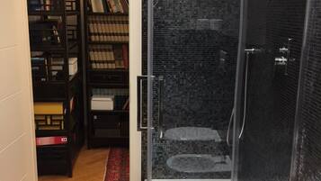 Una ducha a ras de suelo con puerta de cristal, pared de azulejos y suelo de madera.