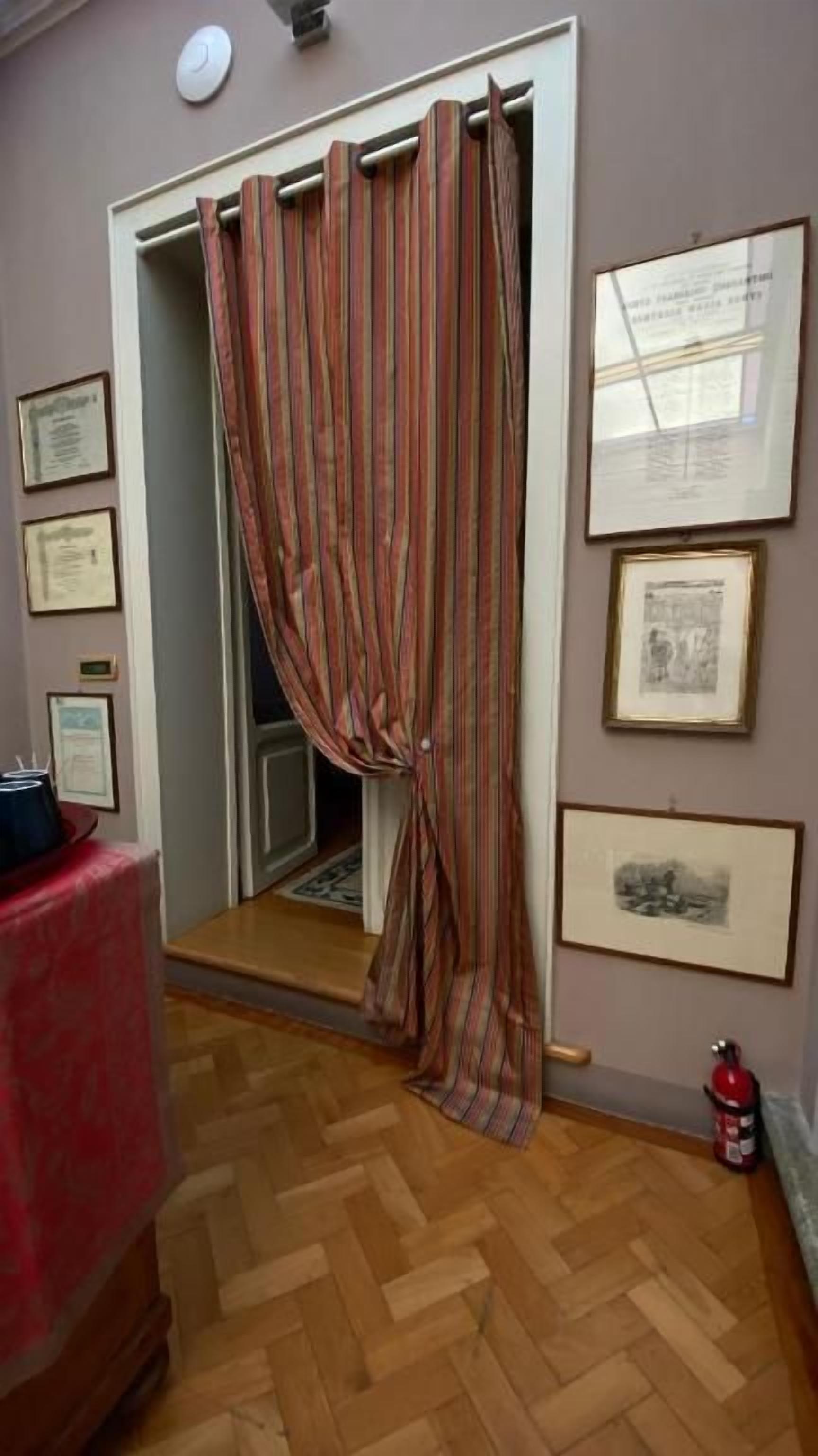 A room with a wooden herringbone floor, a striped curtain, and framed certificates on the wall.