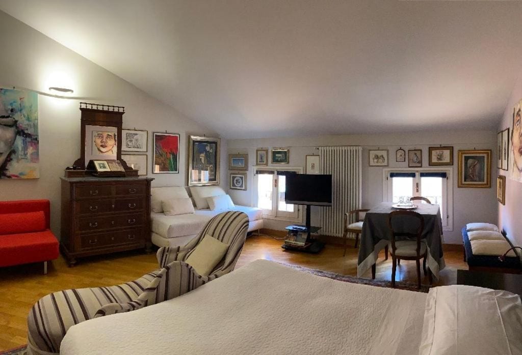 Une pièce comprenant un lit, un canapé rouge, une commode en bois, un téléviseur et divers tableaux encadrés accrochés aux murs.
