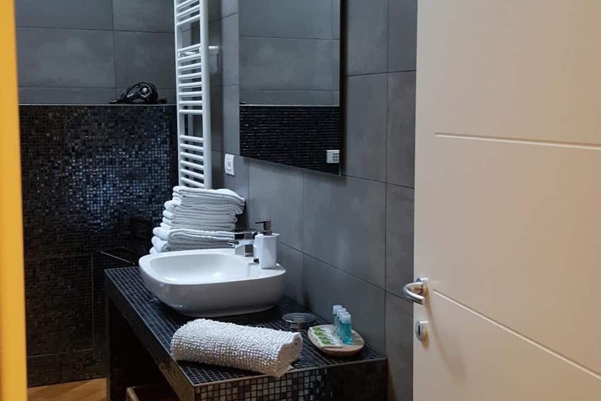 A modern bathroom with a white sink, dark tiled walls, and a mirror above it.