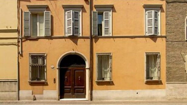 A two-story building with a symmetrical facade, featuring a central entrance with a wooden door and a small balcony above. - A La Maison Ravenna (Ravenna)