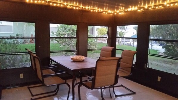 A dining area with a table and chairs, large windows, and string lights.