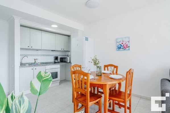 A modern kitchen with white cabinets, a microwave, and a sink. There is a dining table with chairs and a vase with flowers. - Zafiro 28C - Grupo Turis - Calpe, Costa Blanca (Calpe)