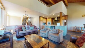 A spacious living area with a sofa, armchairs, a wooden coffee table, and a kitchen in the background.