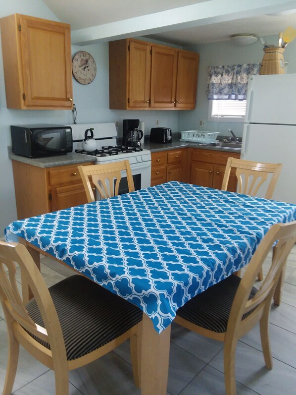 A compact kitchen with wooden cabinets, a microwave, stove, and a dining table with chairs. - Central AC, child safe fenced in yard, 3 minutes to the beach. NO CLEANING FEE
(Hampton)