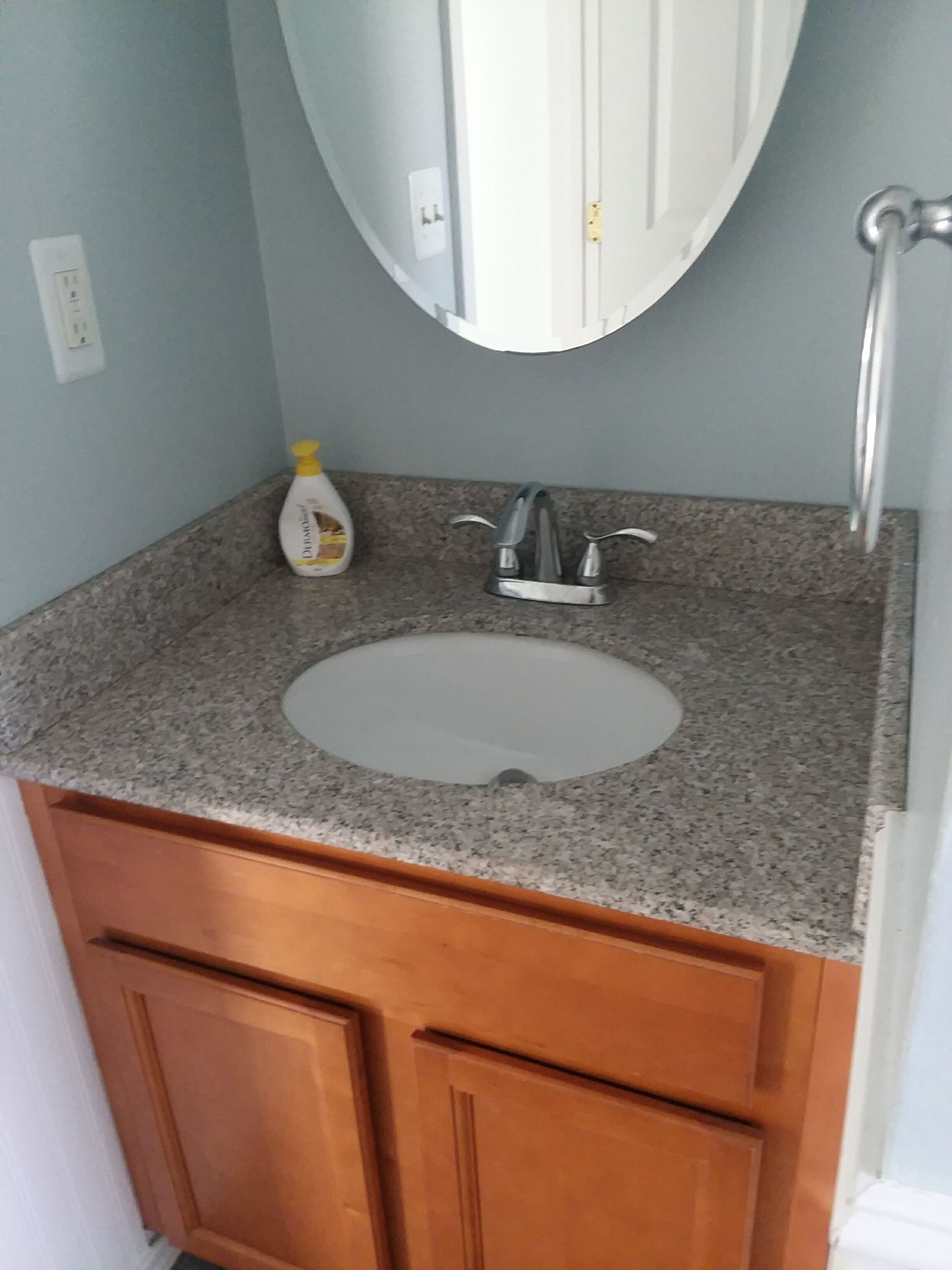 Une salle de bain avec un comptoir en granit, un lavabo blanc, un robinet argenté et des armoires en bois.