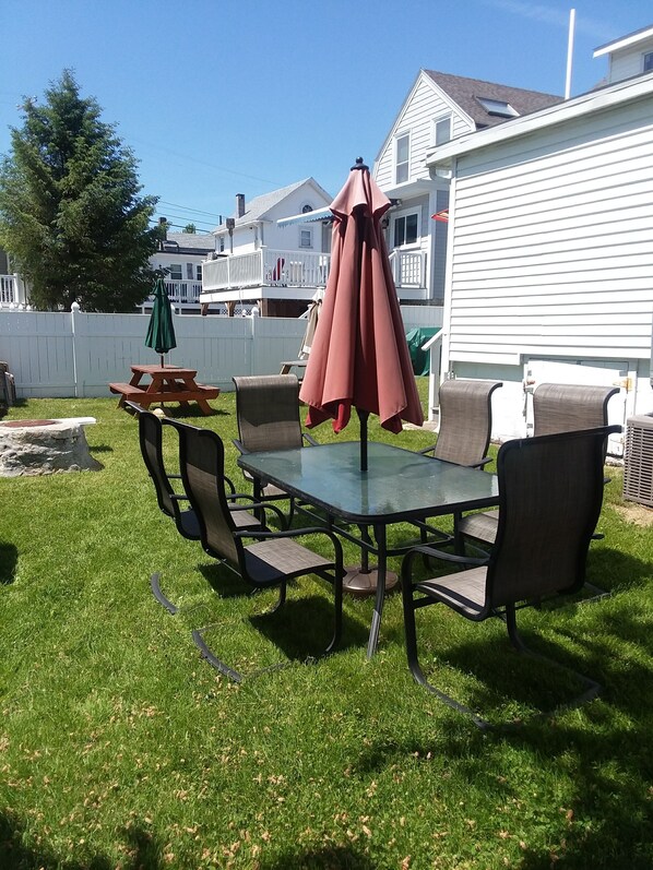 A backyard with a glass table and chairs, a picnic table, and two umbrellas. - Central AC, child safe fenced in yard, 3 minutes to the beach. NO CLEANING FEE
(Hampton)