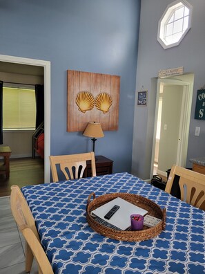 A dining area with a table set for two, a lamp, and a wall-mounted artwork of seashells. - Central AC, child safe fenced in yard, 3 minutes to the beach. NO CLEANING FEE
(Hampton)