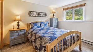 Un dormitorio con cama, mesitas de noche, una ventana con vistas y un elemento decorativo en la pared.