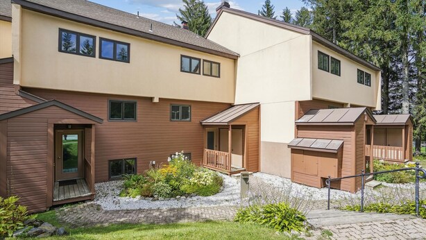 A multi-story residential building with a brown exterior, a small porch, and a gravel pathway leading to the entrance.