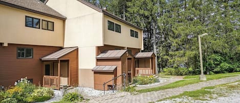 A multi-story building with a flat roof, wooden balconies, and a paved driveway.