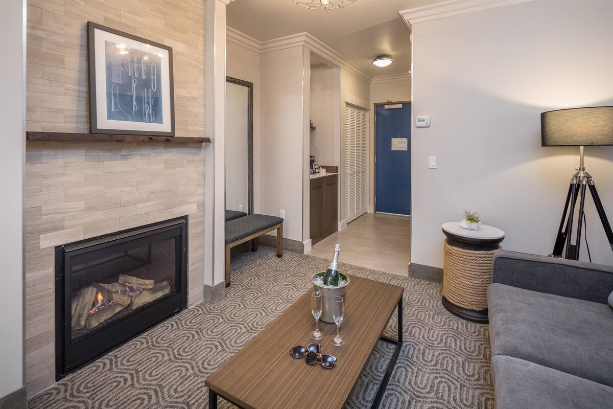 Un salon moderne avec une cheminée, une table basse avec des verres et une bouteille, un canapé et une lampe.