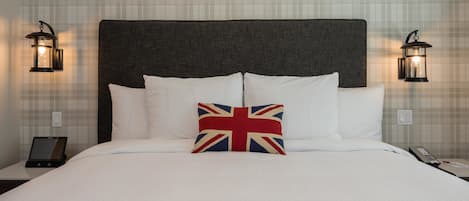 A neatly made bed with white linens and a pillow featuring the Union Jack design. There are two wall-mounted nightstands, each with a black lantern-style light fixture. A tablet is placed on one nightstand.