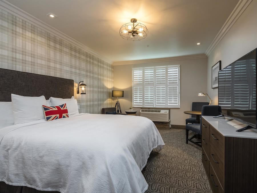 A hotel room with a large bed, a desk, a television, and a window with blinds.