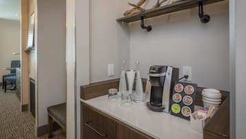 A hotel room with a kitchenette area featuring a coffee maker, glassware, and a coffee pod holder.