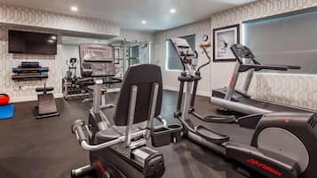 A modern gym with cardio machines, weightlifting equipment, and a large mirror.