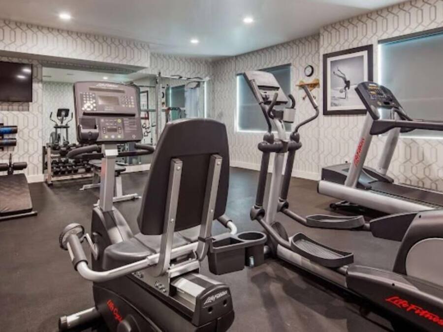 A modern gym with cardio machines, weightlifting equipment, and a large mirror.