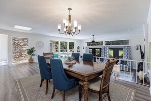 A dining area with a large wooden table, blue upholstered chairs, and a chandelier. - 25 Red Maple: Sea Pines Home, Private Pool, Golf Views, Walk to Beach (Hilton Head Island)