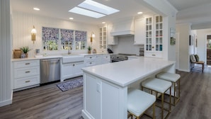 Una cocina amplia con armarios blancos, una isla central y un gran ventanal con cortinas estampadas.