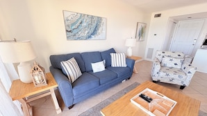 Un salon avec un canapé bleu, une table basse en bois, un fauteuil à motifs et un tableau accroché au mur.