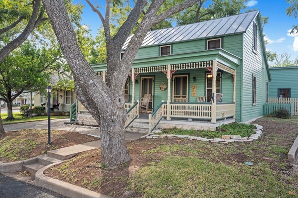 A two-story house with a green exterior, a porch with chairs, and a stone border around the yard.