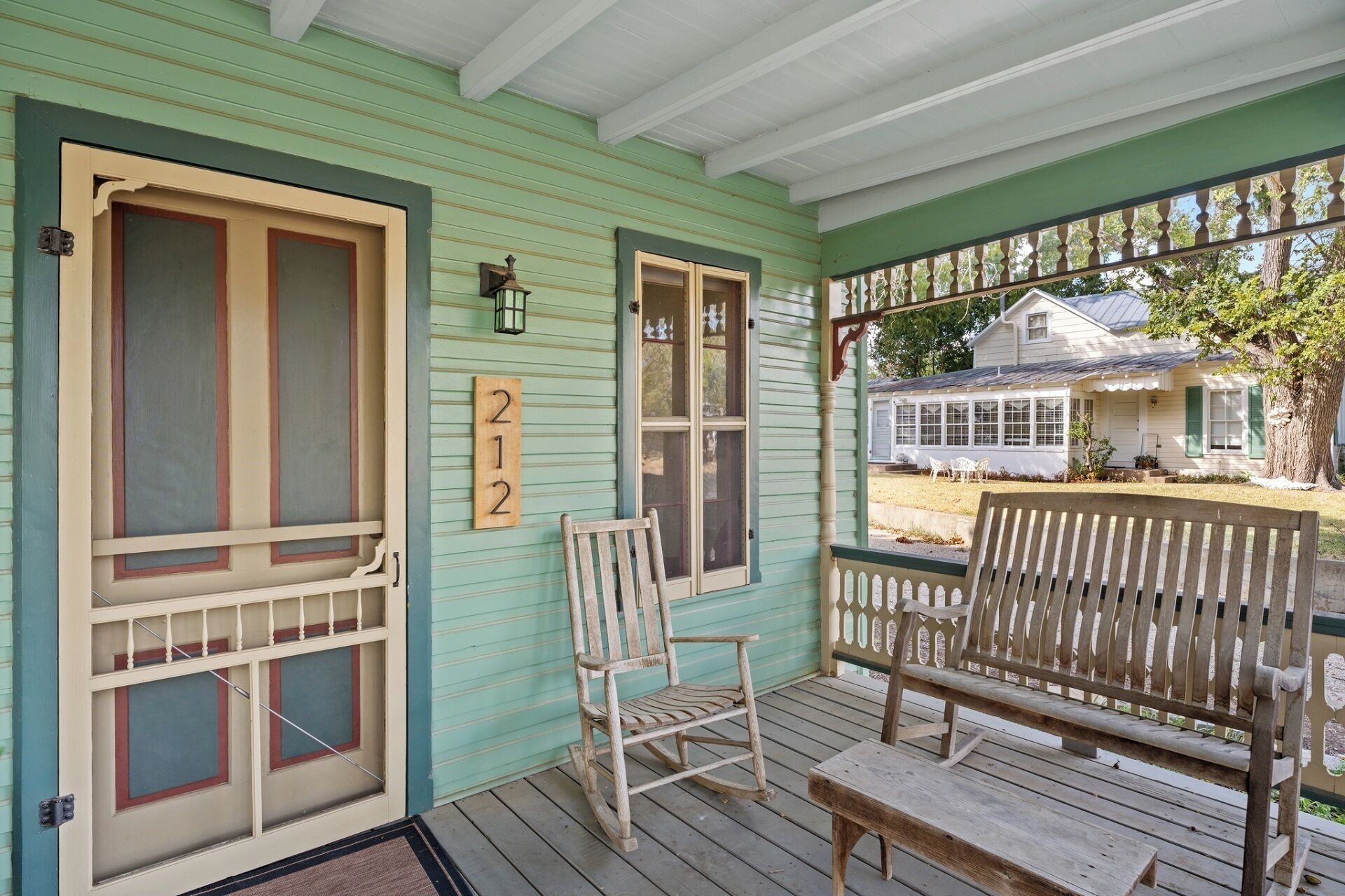 A porch with a wooden bench and a rocking chair, a mailbox, and a house number sign.