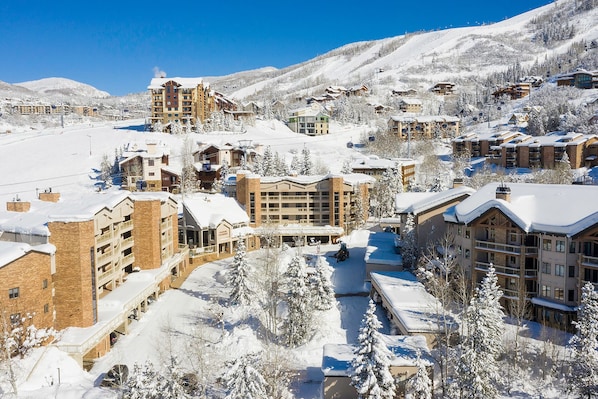 A snow-covered resort with multiple buildings, including a large hotel with a ski lift visible in the background.