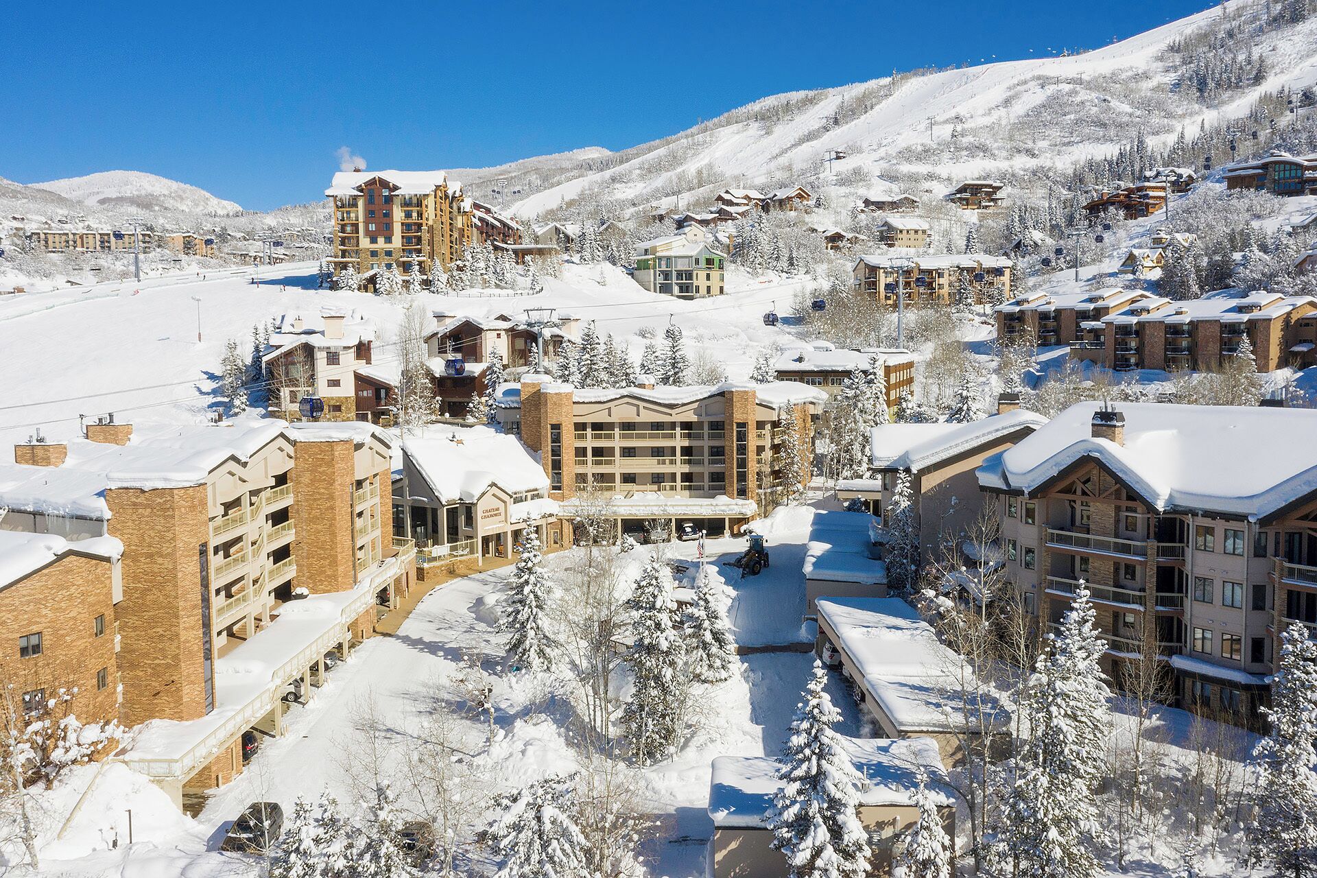 A snow-covered resort with multiple buildings, including a large hotel with a ski lift visible in the background.