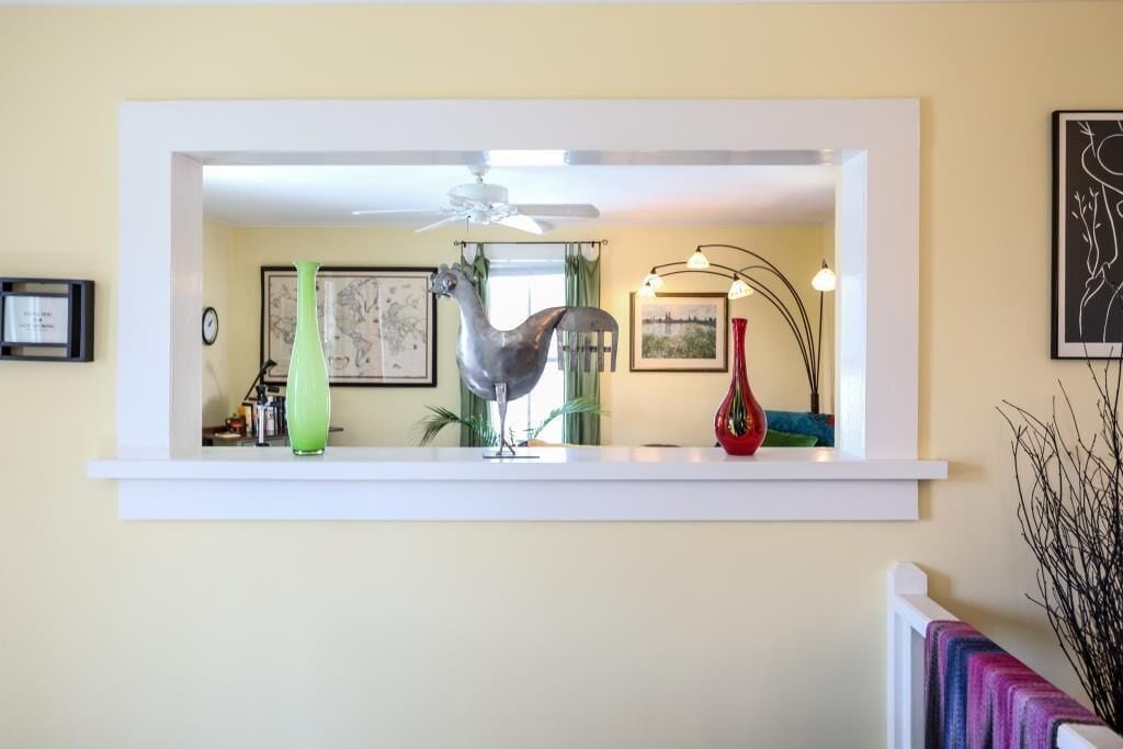 Una habitación con un ventilador de techo blanco, un cuadro enmarcado, un jarrón verde, un jarrón rojo y una escultura de plata.
