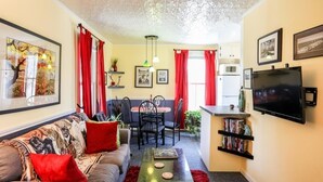 A cozy living room with a sofa, coffee table, and a TV. There is a dining area with a table and chairs, and a kitchen area with a microwave. - Cyclismo - Suite 2 | Close to Main St. | Wonderful Porch (Fredricksburg)