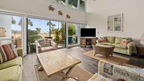 A spacious living room with a large window, a ceiling fan, and a television. - Unit 27, The Sail Away, 2 Bedroom Beach Condo (Panama City Beach)