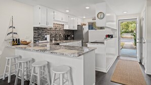 A modern kitchen with white cabinets, a granite countertop, and a built-in island with bar stools. - Unit 27, The Sail Away, 2 Bedroom Beach Condo (Panama City Beach)
